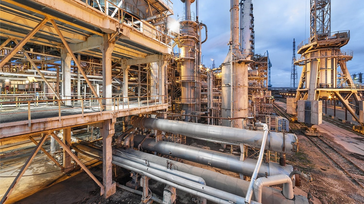 An ammonia production plant with pipes, storage tanks, and cooling equipment in early-morning light, illustrating the industrial process that greener catalyst research seeks to improve.